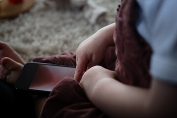 Digital native child as toddler using smartphone when sitting down on the floor indoors. Close-up...