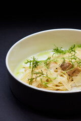 A white bowl filled with spaghetti and meat on a black background