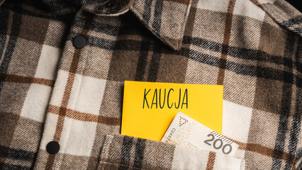  Yellow card with a handwritten inscription "Kaucja", protruding from a brown plaid shirt, next to Polish banknotes PLN (selective focus), translation: deposit