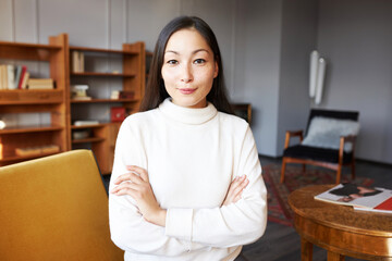 Indoor portrait of charming confident asian woman psychologist in beige sweater smiling at camera...