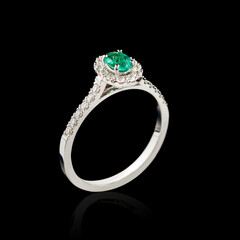 Beautiful white gold ring with diamonds and emerald on a black background