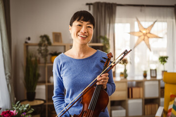 Portrait of mature japanese woman hold violin and smile at home