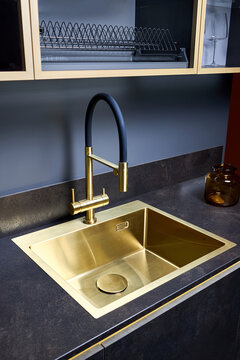 Luxurious interior square golden brass sink and faucet double tap mixer in contemporary modern design with stone marble stoneware countertop black and gold kitchen with sandwatch and glass pot
