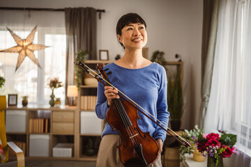 Portrait of mature japanese woman hold violin and smile at home © Miljan Živković
