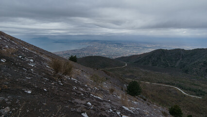 View from the top of Mount Vesuvius down to the city with road through lava field on a cloudy winter day, Naples, Campania, Italy
