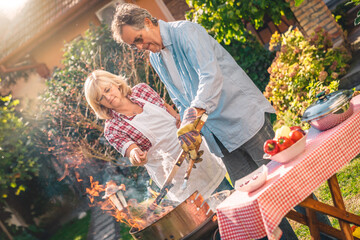 Lovely senior couple preparing barbecue together in backyard. Woman assisting to her husband while...