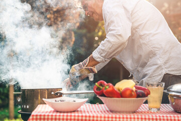 Close up of a male preparing barbecue in backyard. Senior man being busy with roasting meat and...