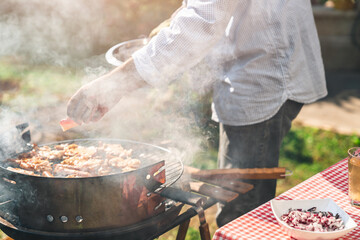 Man preparing meat on the grill in his backyard. Male person picking up roasted meat from the...