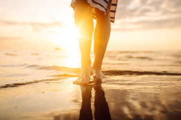 Slim female legs and feet walking along sea water waves on sandy beach. Pretty woman walks at seaside surf. The concept of relax, travel, freedom and summer vacation. - Powered by Adobe