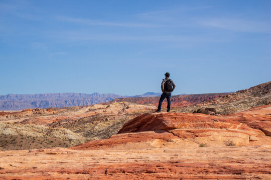 A man is standing and enjoying the spectacular view of Valley of Fire. It is one of geologic wonderland with 2000 year old petroglyphs carved into massive red sandstone formations in the Mohave Desert