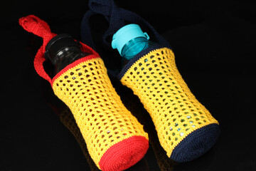 Knitted red, yellow and blue drinking water bottle holder isolated on black background.