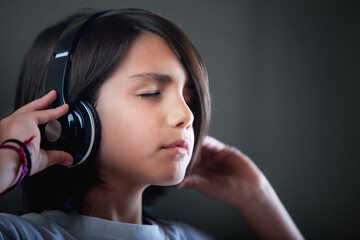 Child listening to music with his headphones with his eyes closed in a moment of peace and...