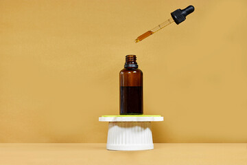Blank amber glass essential oil bottle on podium stand with flying pipette. Skin care concept with natural cosmetics
