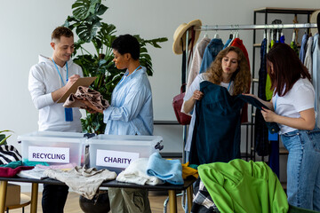 Group of volunteers, young women and man, sorting clothes in charitable foundation for charity donation, recycling. Concept of textile pollution, conscious consumption. Ecology, sustainable lifestyle