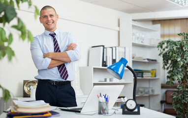 Portrait of male businessman who is standing near his workplace in the office