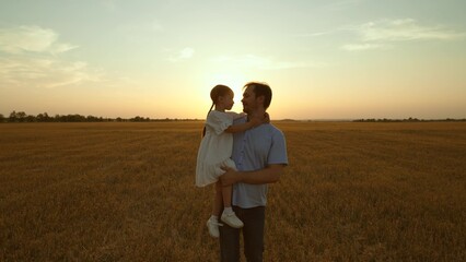 Father holding kid in arms in field at sunset. Happy cheery parent child kid strolling moving going...