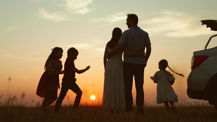 Family at sunset near car silhouettes. Kids children with ball running around parents enjoying...