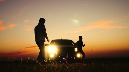 Father son dancing at sunset near car silhouettes. Man dad boy kid child at orange sunset near car with headlights on having fun with music giving free rein to feelings partying at nature field park