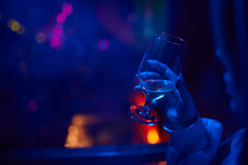 A woman holds a cocktail in her hand, with her fingers wrapped around the glass - obrazy, fototapety, plakaty