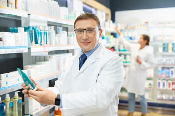 In pharmacy, male specialist holds in hands and presents shows new effective remedy for moisturizing delicate skin of children