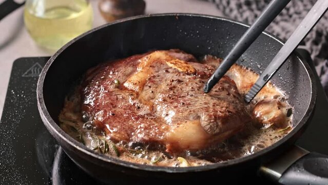 A chef cooks a beef steak on a pan in the kitchen and turns it to the other side, close-up. Process of making delicious steak.