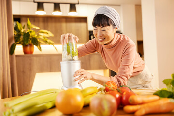 A happy japanese woman is blending smoothie in kitchen.