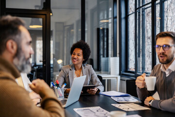 A multicultural manager is sitting at boardroom with her coworkers and collaborating on a project.