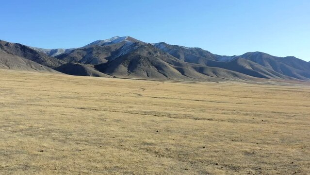 A vast, empty desert with a mountain range in the background. The sky is clear and blue, and the sun is shining brightly. The scene is peaceful and serene