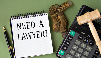 NEED A LAWYER? - words in a notepad against the background of a calculator and a judge's gavel
