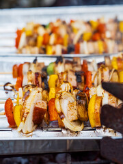 Close up of skewers with sausages and colorful peppers being cooked on a foil tray in a backyard. Summer barbecue easy food concept. Selective focus. Party mood and feel.