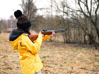 Teenager girl in yellow jacket with small caliber gun in a country side setting. Sport and hobby....