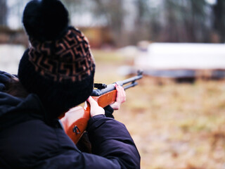 Young teenager girl win long nails aiming small caliber rifle. Selective focus. Nature area....
