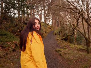Young teenager girl in yellow jacket on a walk in a dense forest. Travel and tourism concept....