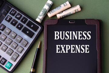 BUSINESS EXPENSE - words in an electronic notebook on the background of a calculator and banknotes