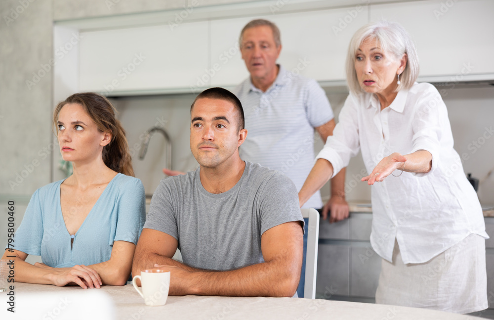 Wall mural elderly parents make claims to young couple in home kitchen