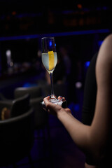 A woman holds a cocktail in her hand, with her fingers wrapped around the glass