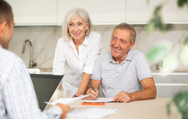 Couple of elderly man and woman discussing deal with male salesman in kitchen home