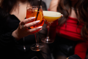 A woman holds a cocktail in her hand, with her fingers wrapped around the glass