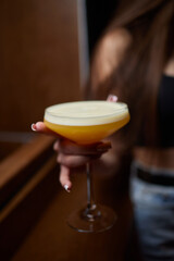 A woman holds a cocktail in her hand, with her fingers wrapped around the glass