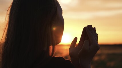 Woman praying with folded hands at sunset silhouette. Religious pious orthodox christian spiritual...