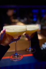 A woman holds a cocktail in her hand, with her fingers wrapped around the glass