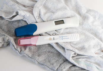 Close up of two positive pregnancy tests on baby clothes