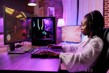 Woman in brick wall living room playing SF video game on gaming PC at computer desk late at night. Tired gamer girl battling hostiles in online multiplayer futuristic shooter