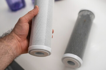 Man holding new carbon filter for reverse osmosis purification water system, while dirty lies on...