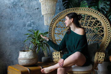 Girl sitting in balinese style armchair in tropical interior and touching plant with love and care