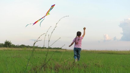 Overjoyed little girl child running with flying kite at green grass field enjoy happy childhood. Cute female kid playing outdoor flight toy entertainment joy with positive emotion at summer meadow