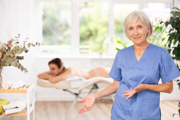 Fototapeta premium In spa office there is elderly woman nurse dressed in medical uniform, suit. Advertising poster, banner for salon of cosmetology and massage services