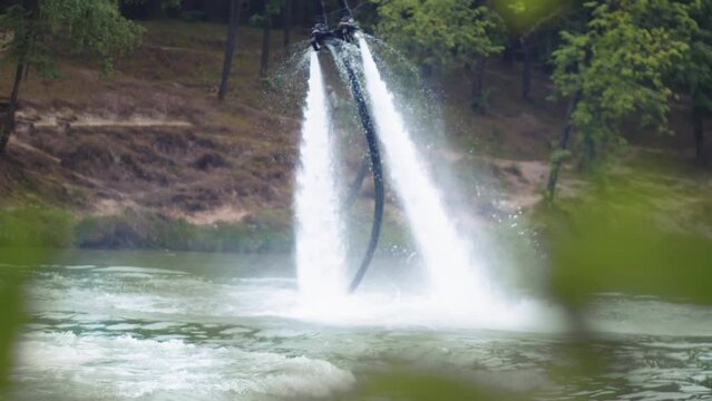 Man on a flyboard hovers above the river, against the backdrop of trees. He deftly balances thanks to the water's pressure. Long shot. Slow motion.