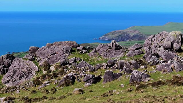 Tracking aerial shot of mountain peak and rocky outcrop revealing Welsh coastline in distance