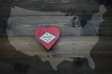 wooden heart with national flag of arkansas state near united states of america map on the wooden background.